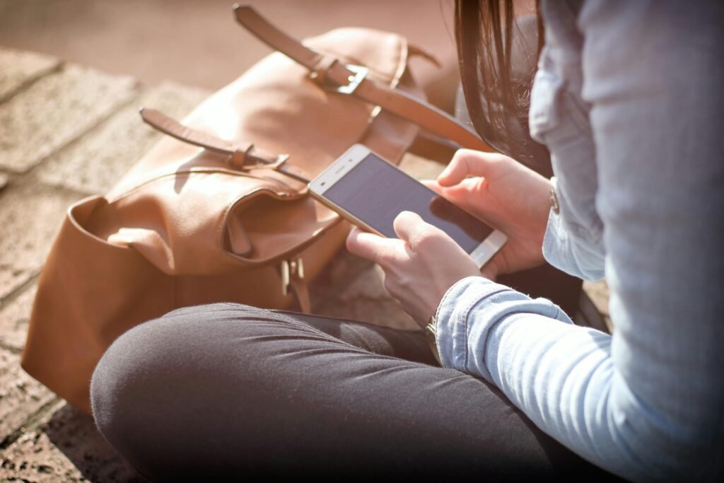 Woman sitting with smartphone and brown bag in sunlight.